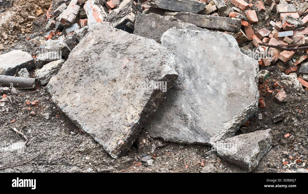 Due grandi blocchi di calcestruzzo poggiano su un mucchio di macerie e detriti in un cantiere di costruzione o demolizione attivo. Foto Stock