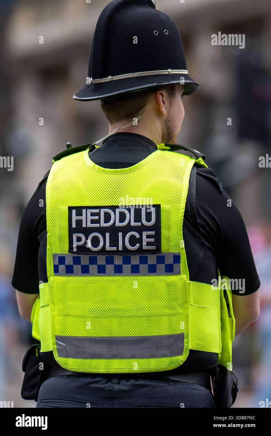 Un ufficiale di polizia maschile si trova di fronte alla telecamera con le parole Heddlu/Police sulla schiena. Foto Stock