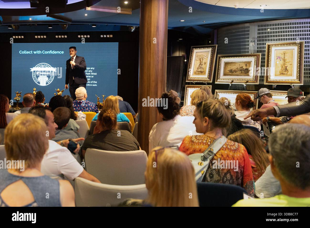 I passeggeri partecipano a un'asta d'arte di una nave da crociera mentre un banditore presenta opere d'arte incorniciate a un pubblico seduto in un luogo in stile teatro a bordo. Foto Stock