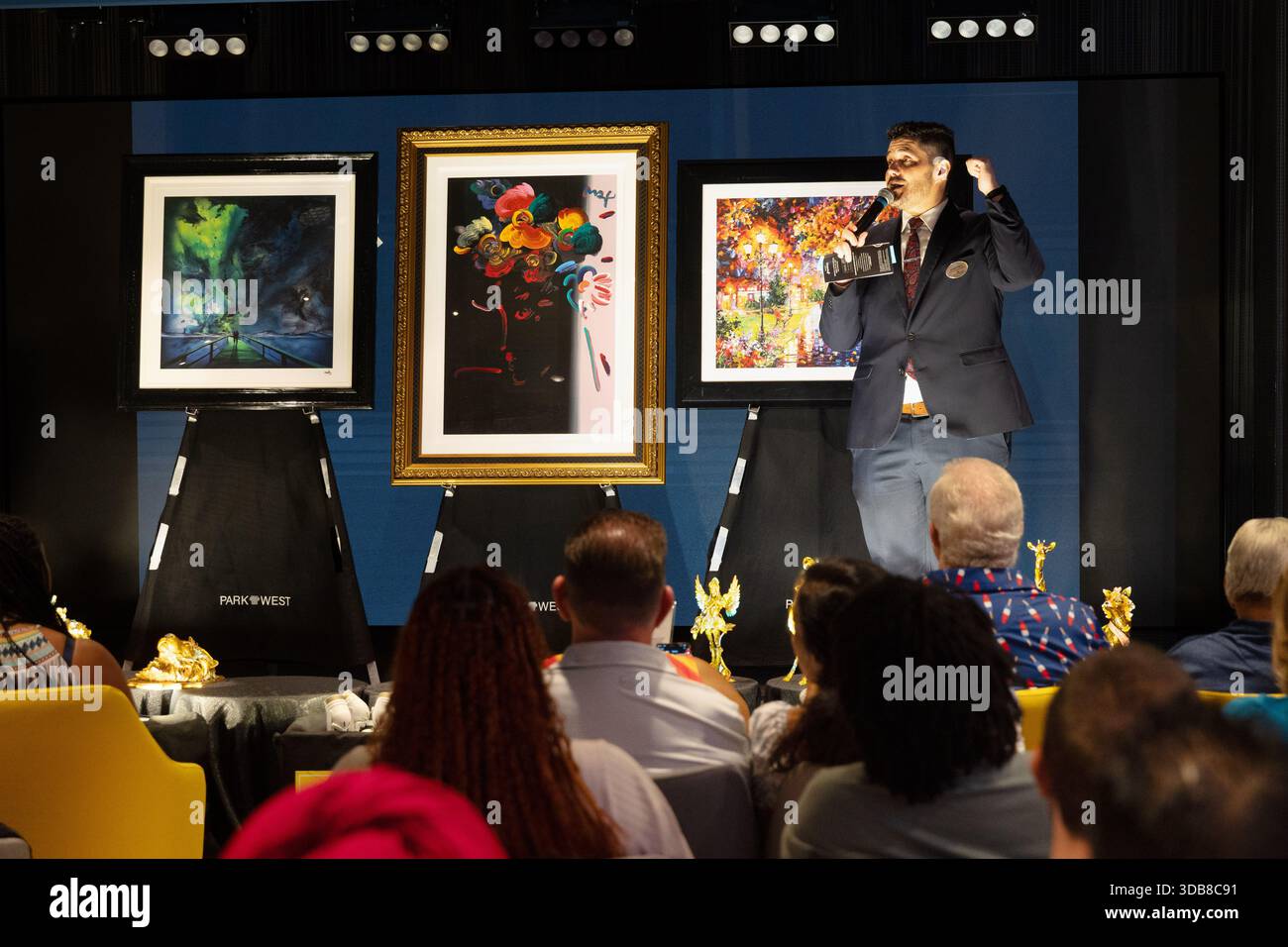 I passeggeri partecipano a un'asta d'arte di una nave da crociera mentre un banditore presenta opere d'arte incorniciate a un pubblico seduto in un luogo in stile teatro a bordo. Foto Stock