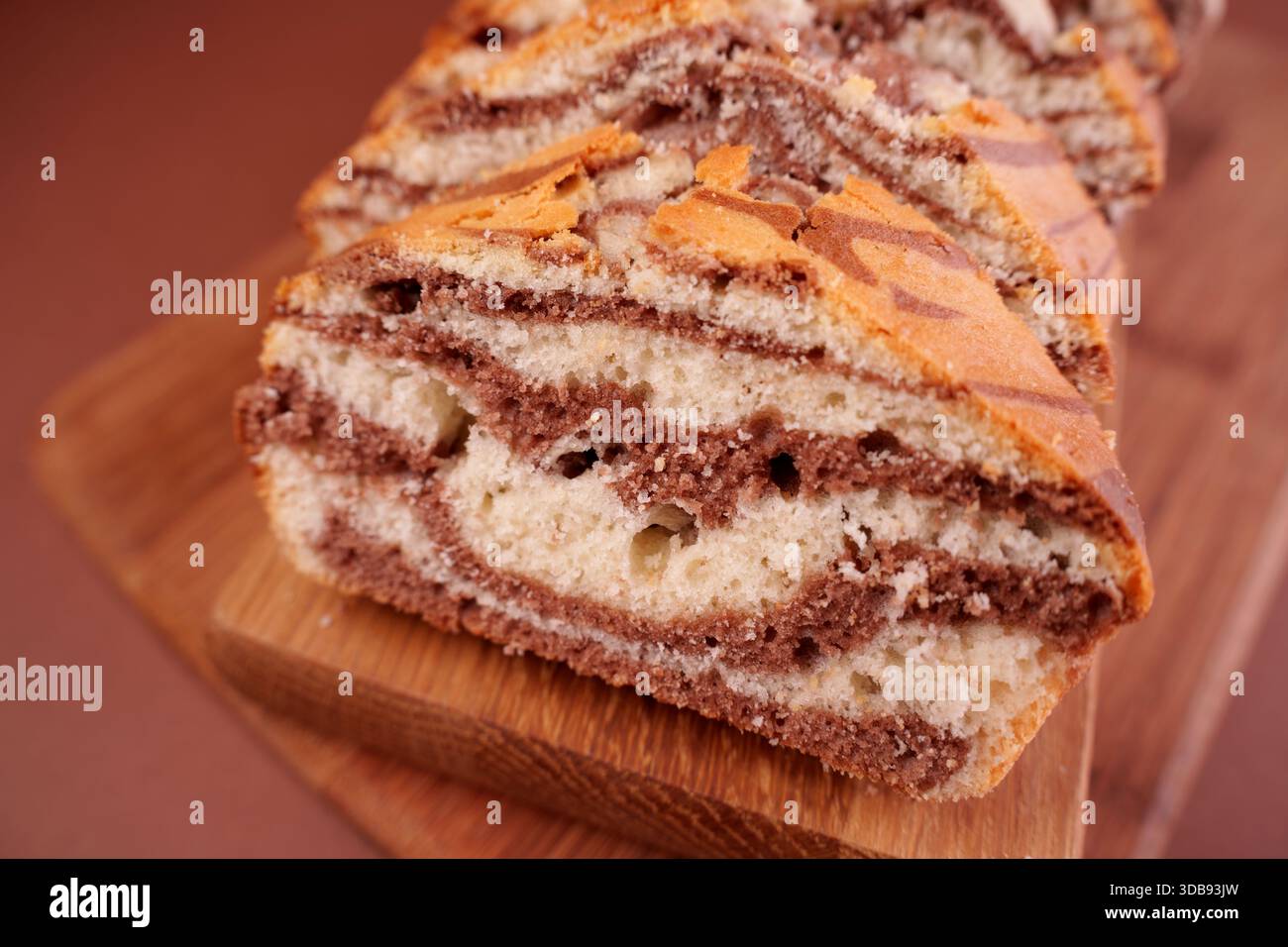 primo piano di torta in marmo affettata con ricchi vortici di vaniglia e cioccolato su un tagliere in legno con fondo morbido, morbidezza, brownie, yumm Foto Stock