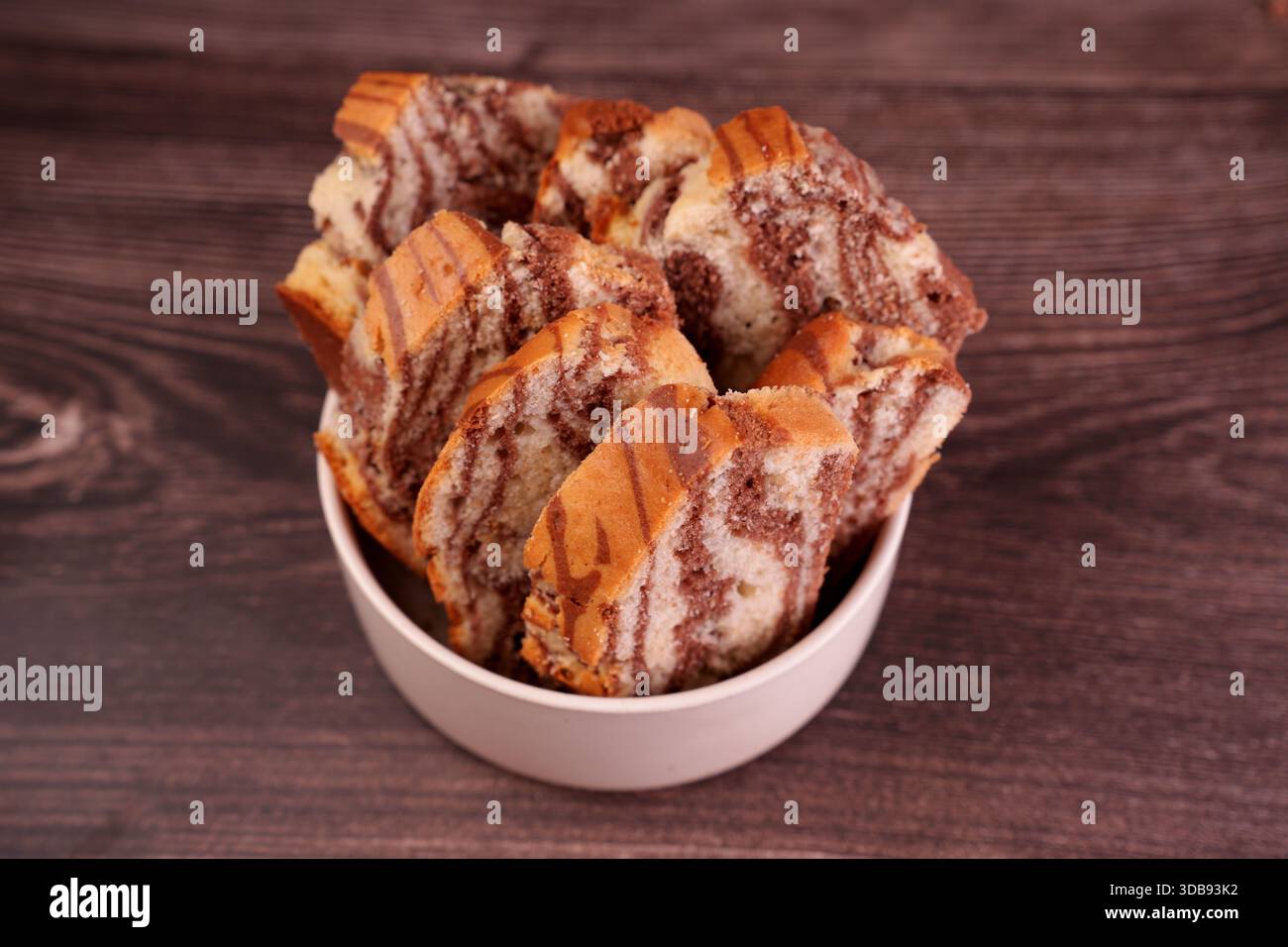 vista ravvicinata delle fette di torta di marmo disposte ordinatamente in una ciotola bianca su una superficie in legno testurizzato, che mostra un delizioso motivo a turbolenza di cioccolato a. Foto Stock