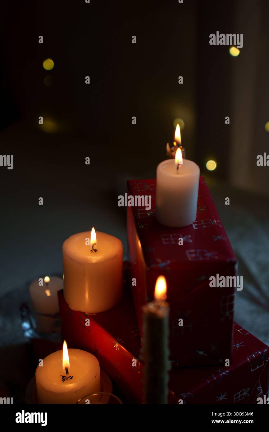 un ambiente accogliente a lume di candela con candele bianche accese su regali avvolti, che creano un'atmosfera calda e festosa con luce soffusa e sfarfallio sullo sfondo scuro Foto Stock