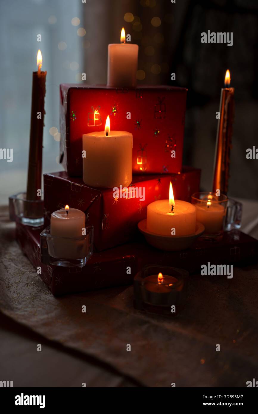 caldo bagliore di candele in cima a scatole regalo rosse con morbido bokeh in un ambiente interno accogliente, che evoca lo spirito delle vacanze e la tranquillità con fiamme scintillanti Foto Stock