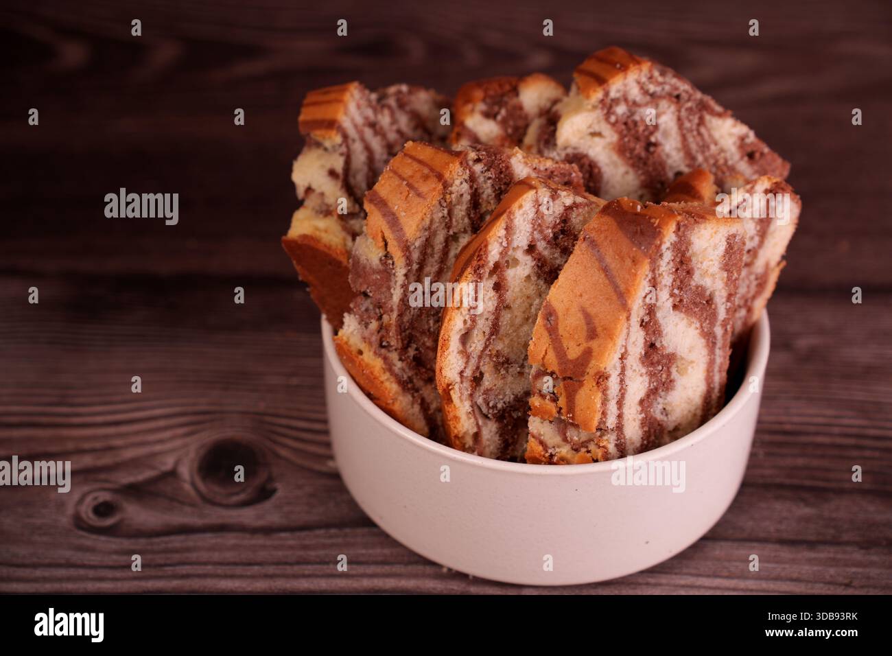 primo piano di una ciotola riempita di torta di marmo appena tagliata che rivela intricati vortici di cioccolato e vaniglia contro un ricco backgrou di legno testurizzato Foto Stock