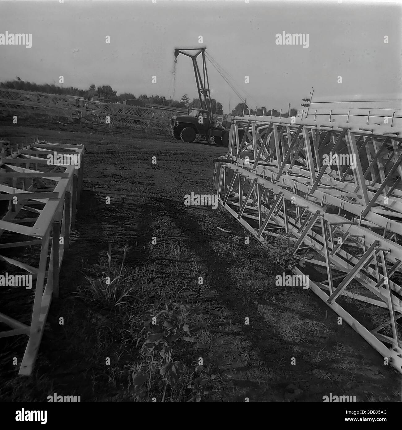 1970 anni URSS. Regione di Donetsk. Costruzione di linee elettriche strategiche ad alta tensione da 750 kV. Vista del cantiere logistico in cui vengono immagazzinate massicce sezioni reticolari in acciaio delle torri di trasmissione prima del montaggio. Una gru per camion sovietica sta operando sullo sfondo tra le strutture metalliche. Il terreno fangoso con le tracce degli pneumatici indica il traffico intenso attivo. Un documentario storico girato che illustra la portata dello sviluppo delle infrastrutture industriali nella pacifica steppa del Donbas. Foto Stock