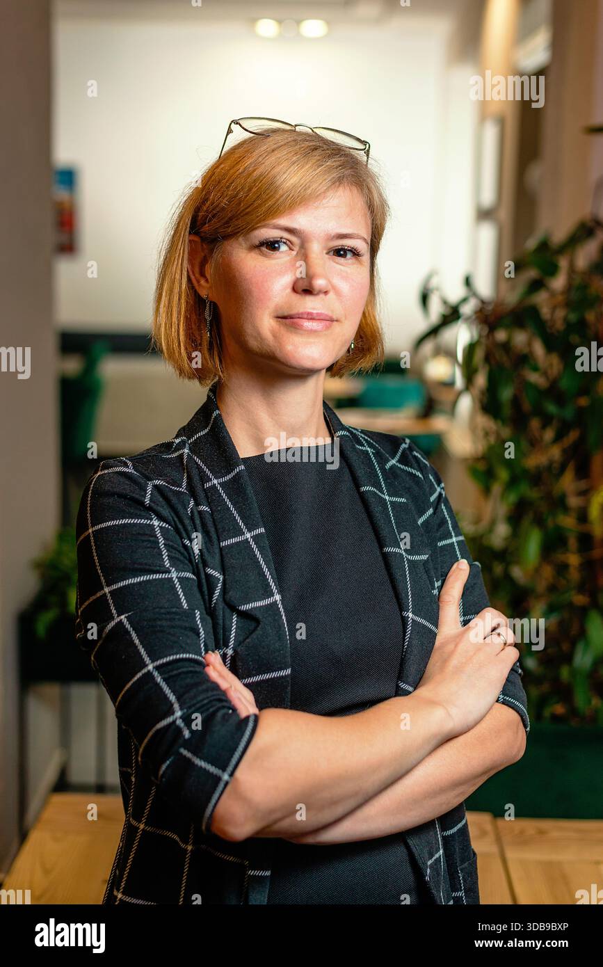 La donna sta in piedi con le braccia incrociate in uno spazio di lavoro elegante. Foto Stock