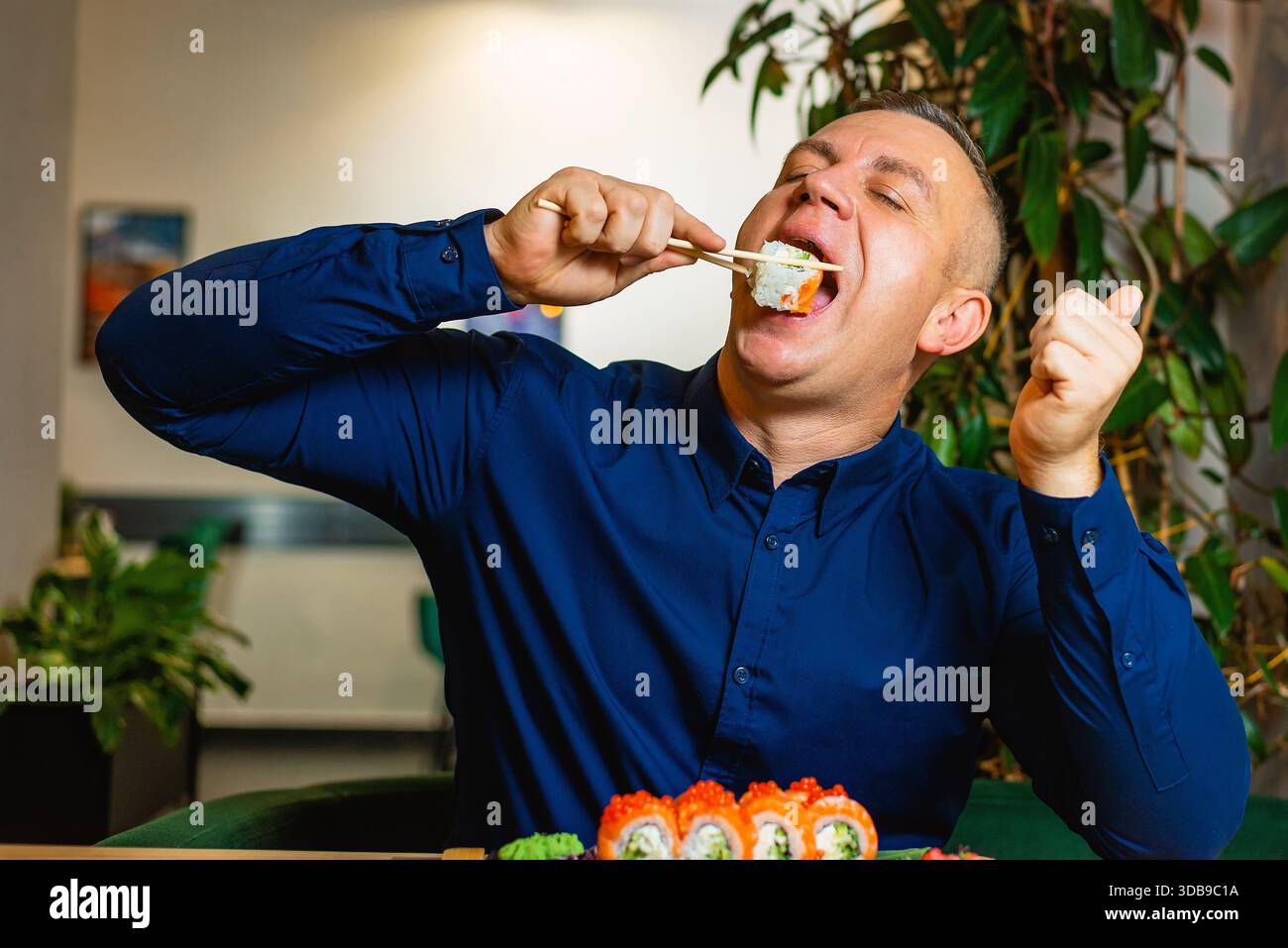 Un uomo vivace morde in un sushi roll, esprimendo gioia ed entusiasmo. Foto Stock