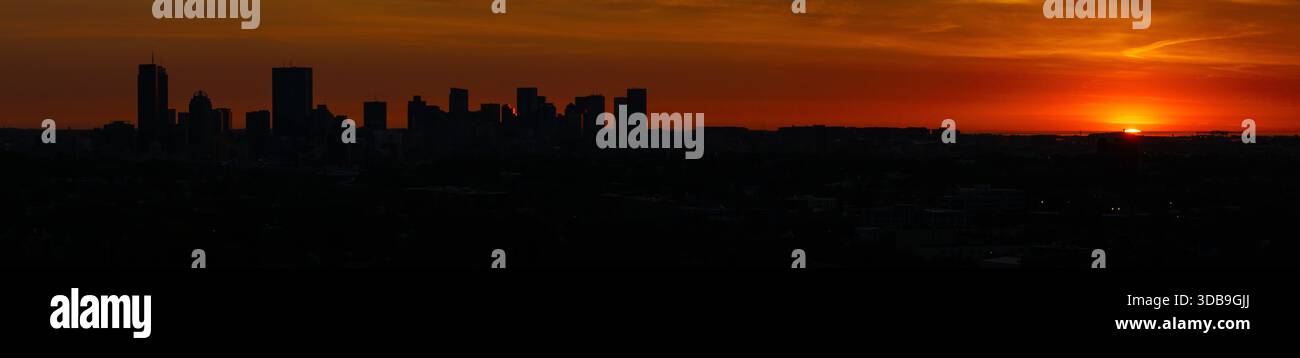 Veduta aerea dello skyline di Boston che si staglia contro un tramonto infuocato, dove il sole si tuffa sotto l'orizzonte creando un contrasto drammatico, Boston, massa Foto Stock