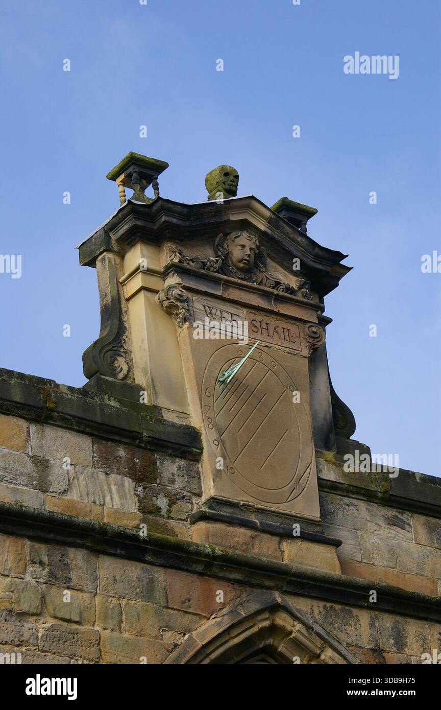 Vecchia meridiana in pietra sulla facciata della chiesa di Ognissanti, Kedleston, Derbyshire, Regno Unito; abbiamo inciso sopra un teschio di pietra scolpita Foto Stock