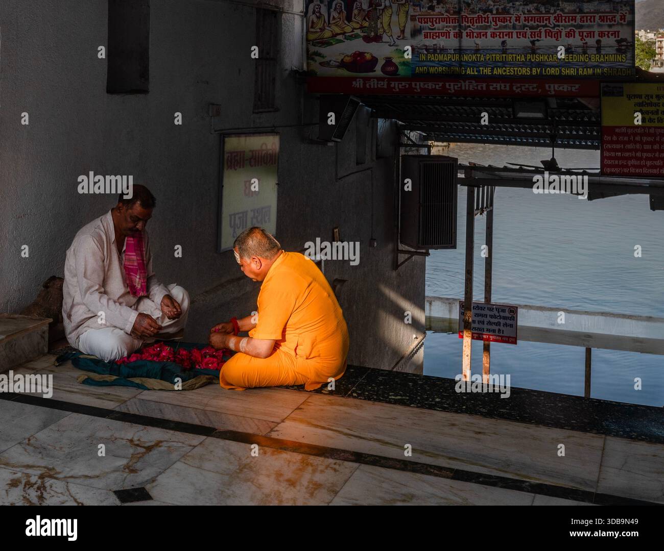 Pellegrino che parla con un sādhu sui ghati del lago Pushkar, Rajasthan, India – Un momento di spiritualità e tradizione in uno dei più sacri dell’India Foto Stock