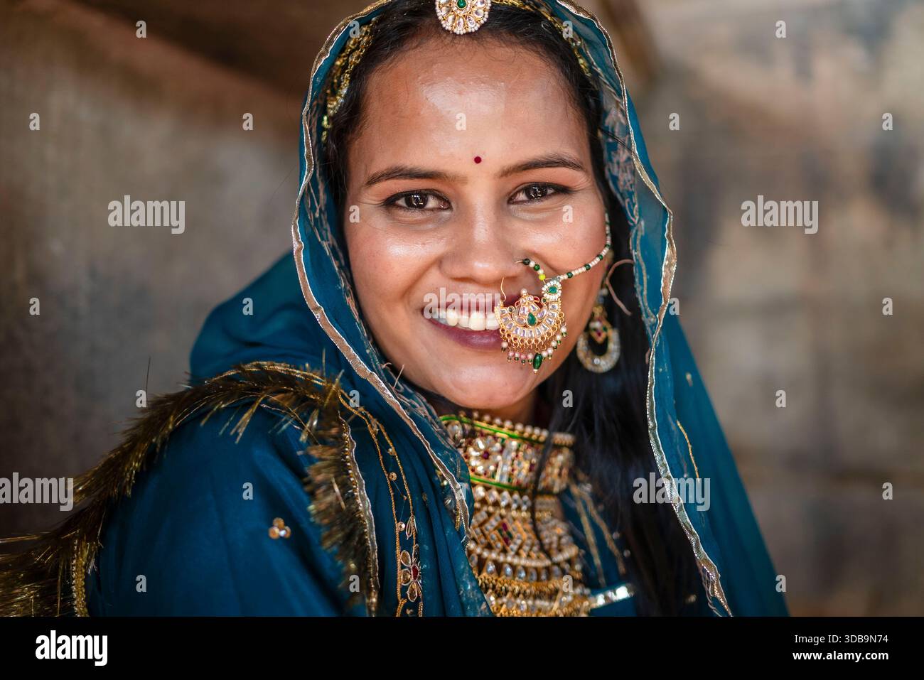 Sposa indiana sorridente che indossa abiti tradizionali e gioielli ornati, ritratto in luce naturale. Foto Stock
