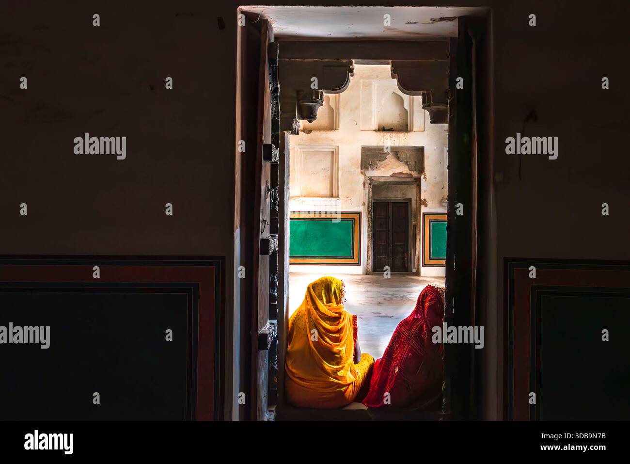 Momenti tranquilli a colori: Due donne in saris appoggiate sui gradini di una porta indiana. Foto Stock