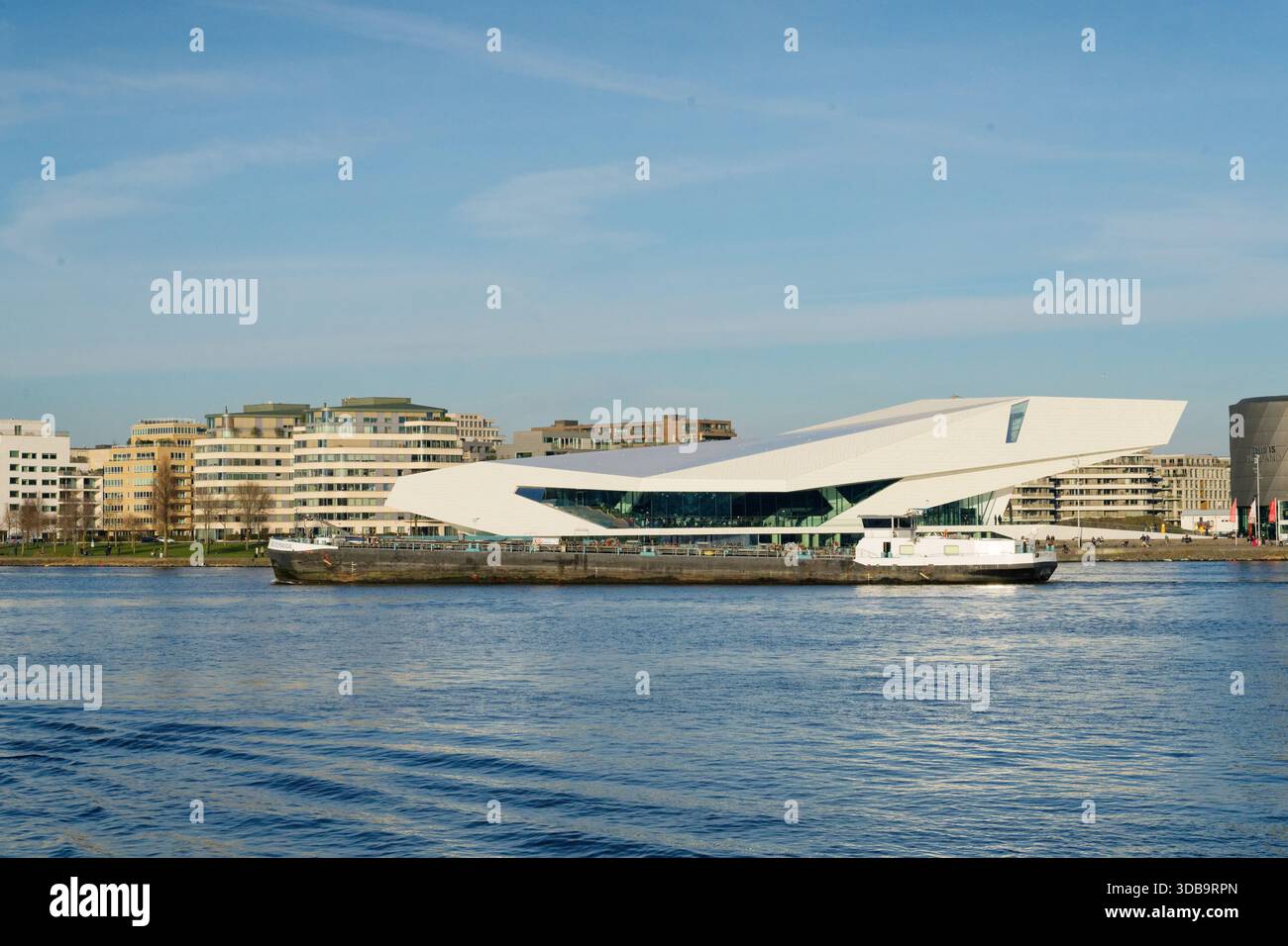 Un suggestivo edificio moderno si trova lungo il lungomare, che riflette il suo design contemporaneo sullo sfondo della vita cittadina e dei cieli azzurri. Foto Stock