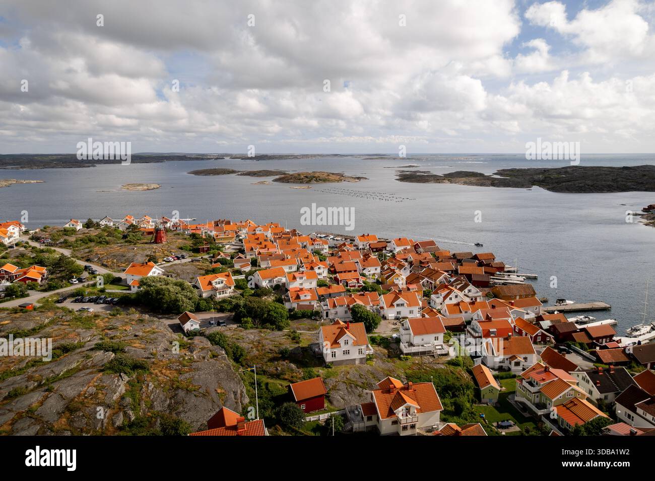 Vista aerea delle case dal tetto rosso incastonate tra affioramenti rocciosi, in contrasto con il vasto mare blu e le isole sparse sotto un cielo nuvoloso, Mollosund, Foto Stock