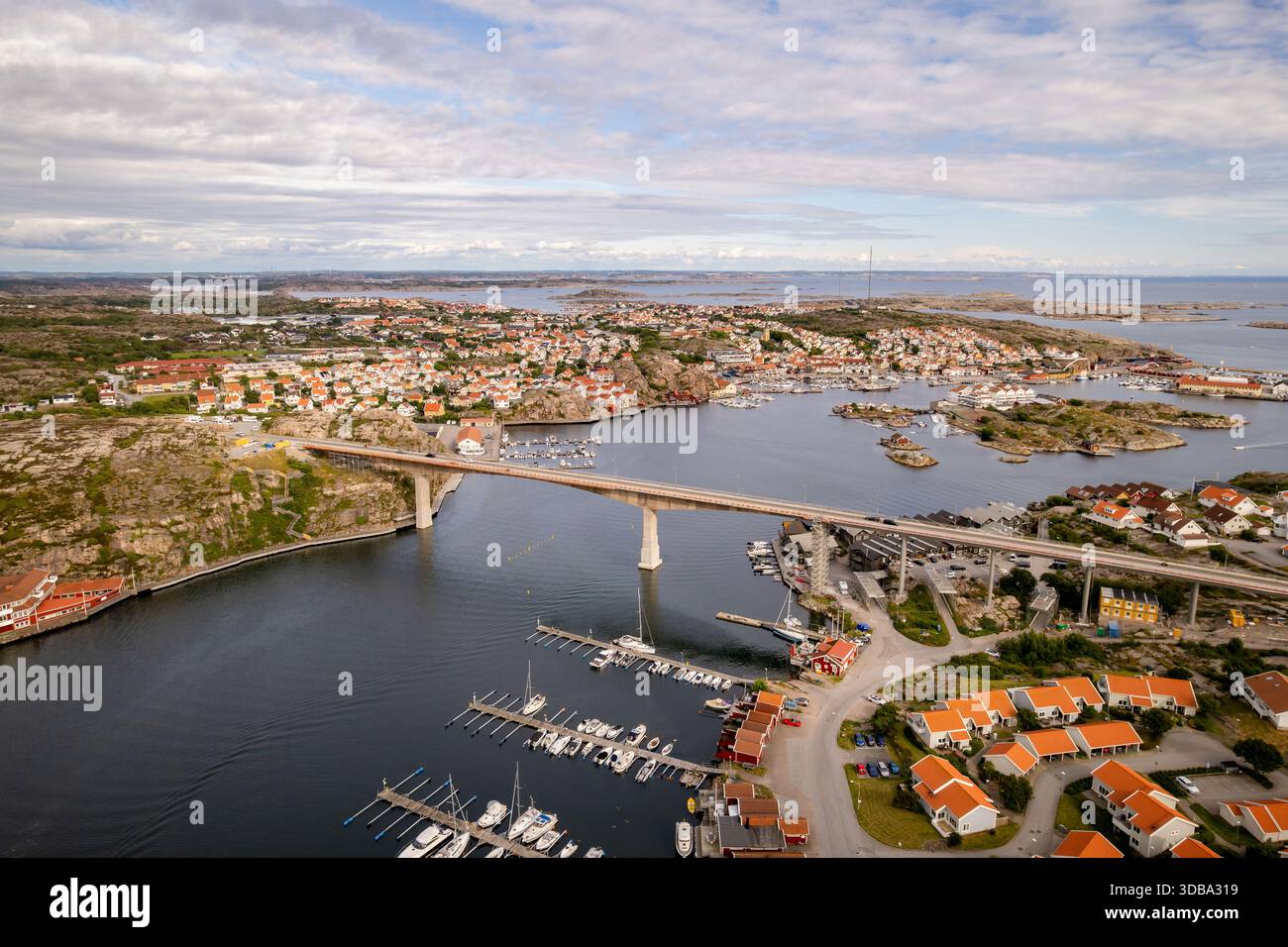 Veduta aerea di un ponte che collega le coste rocciose punteggiate da case dal tetto rosso, barche che ormeggiano nel porto sotto un vasto cielo, Smogen, Vastra Gotaland C. Foto Stock