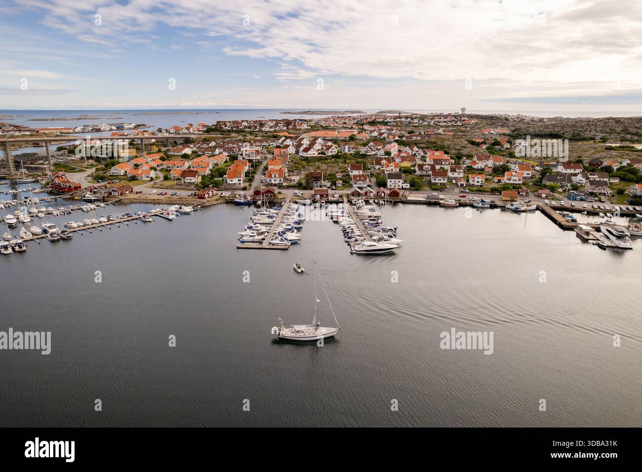 Vista aerea di un tranquillo porto pieno di yacht e barche, incorniciato da case dal tetto rosso e da un ponte sotto un vasto cielo, Smogen, Vastra Gotaland County Foto Stock