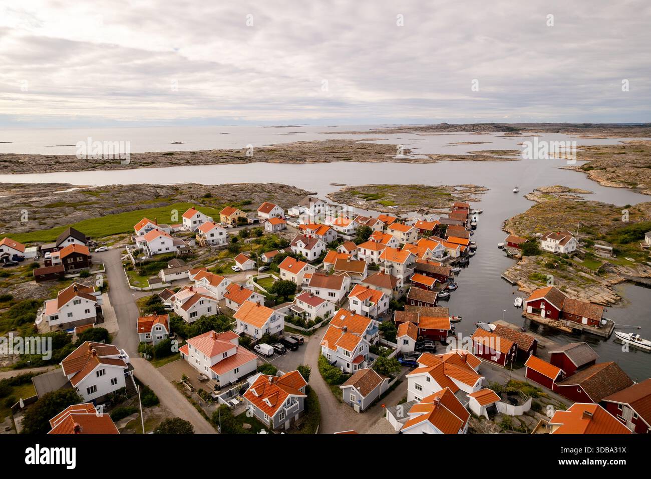 Vista aerea delle case dal tetto rosso annidate lungo la costa rocciosa, dove il villaggio incontra il mare sotto un vasto cielo nuvoloso, Smogen, Vastra Gotaland Foto Stock