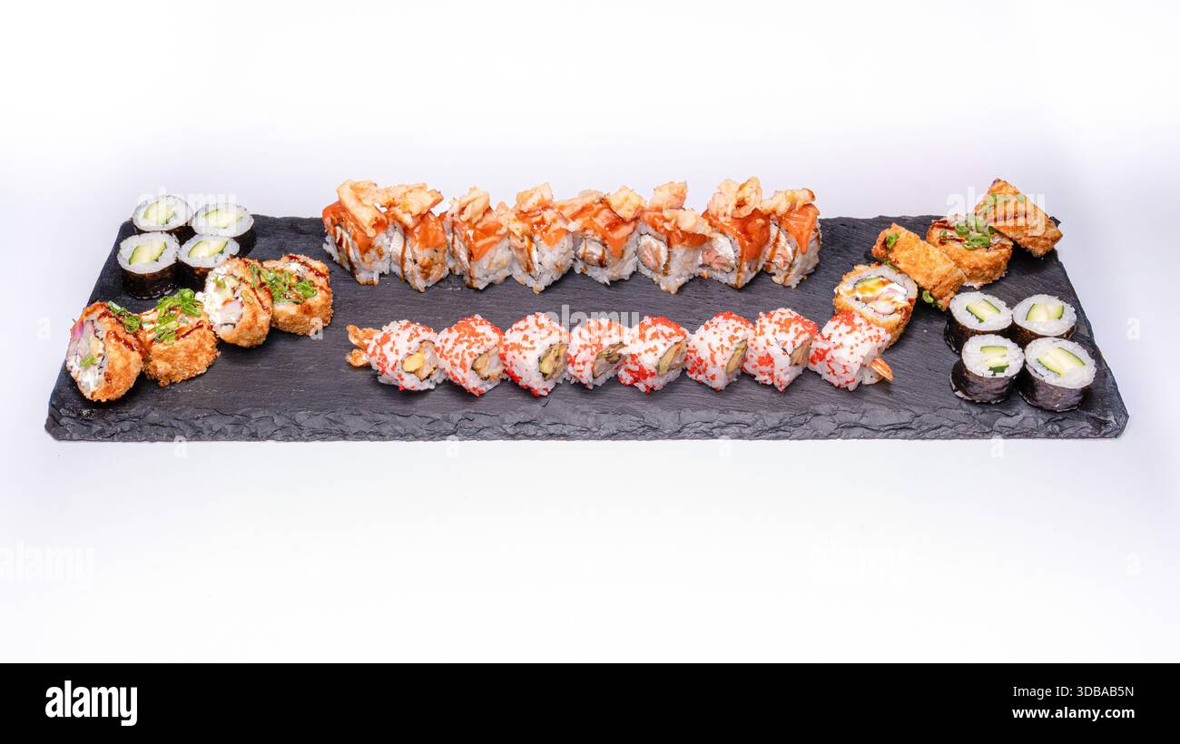 Ampio piatto misto di sushi con uramaki, maki e sushi fritti servito su una tavola di ardesia nera isolata su sfondo bianco. Foto Stock