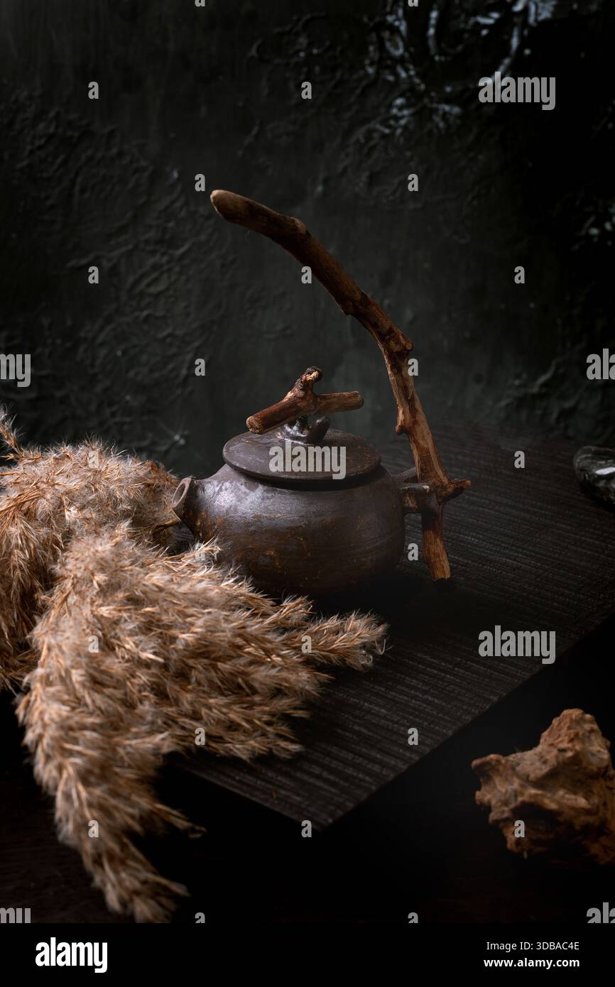 Cerimonia del tè cinese. Teiera nera in ceramica tradizionale fatta a mano con manico in legno sul tavolo da tè scuro. Autunno Vibe. Fiori di canne secchi affiancati. Co Foto Stock