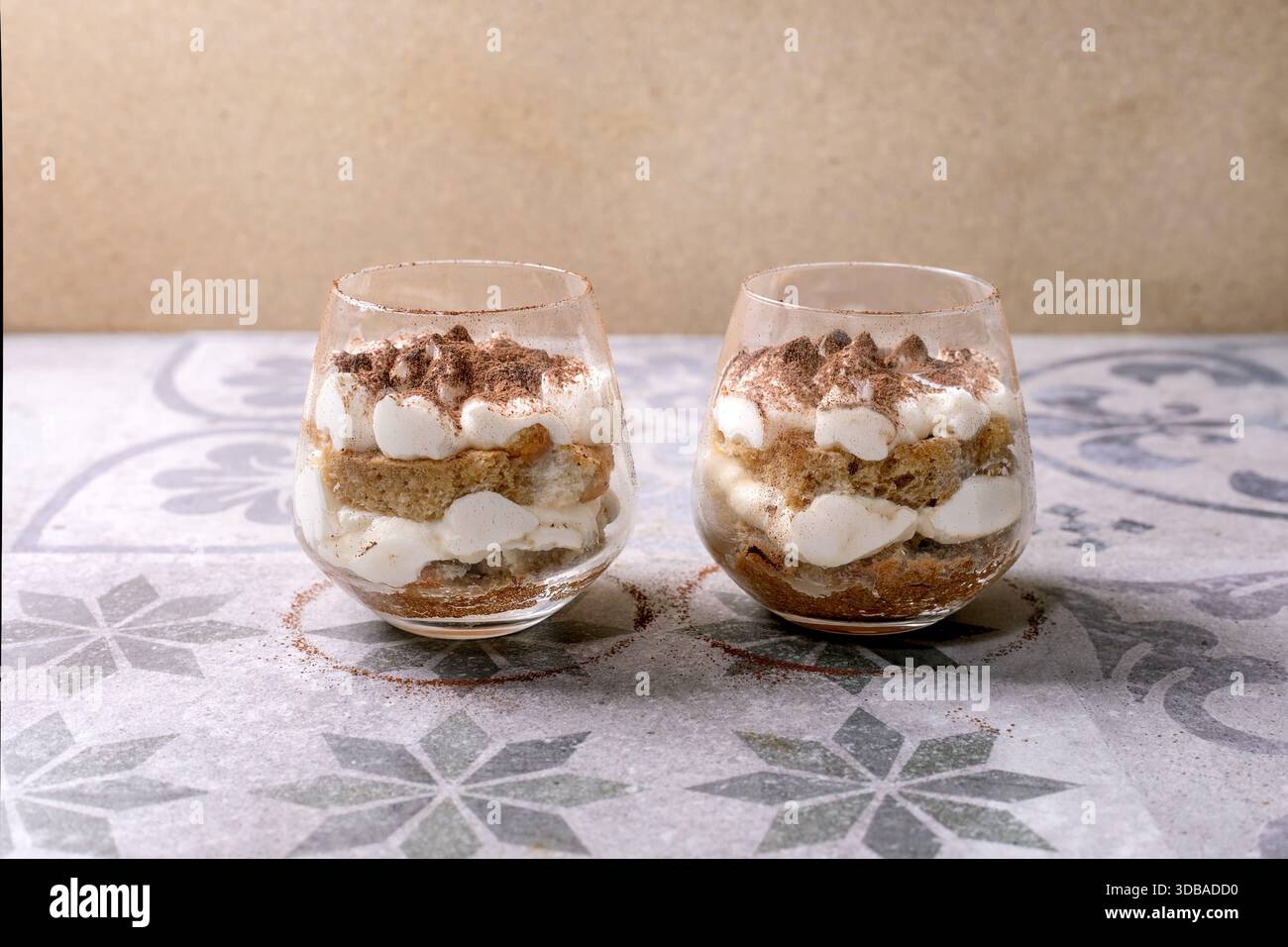 Classico dessert italiano al tiramisù servito in due bicchieri. Strati di spugna imbevuta di caffè e mascarpone cremoso, spolverato con cacao in polvere. Inserito su patt Foto Stock