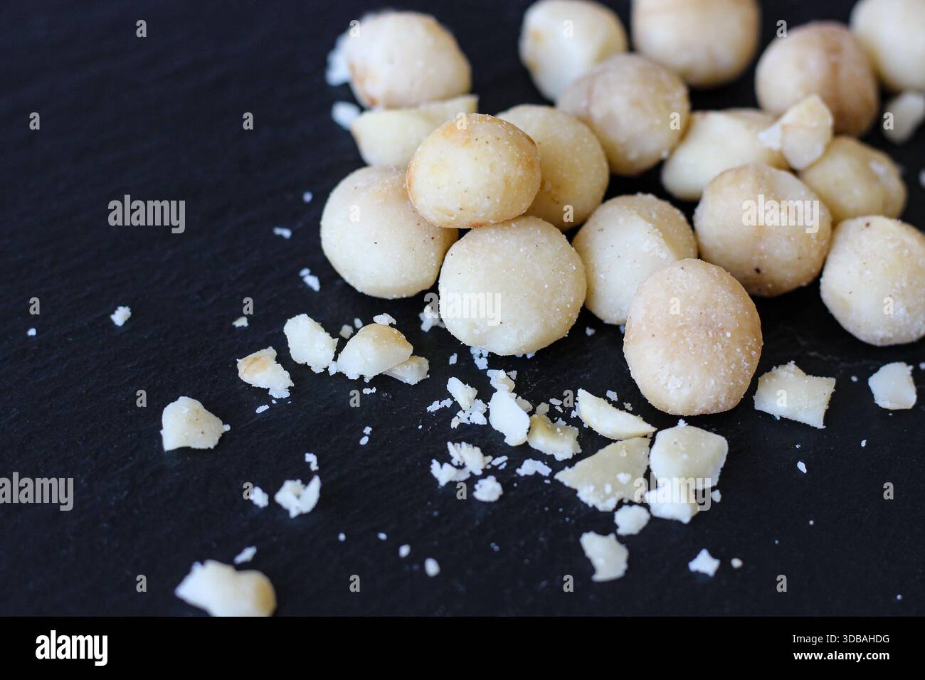 Noci di macadamia con briciole su una superficie di pietra scura. Vista ravvicinata degli ingredienti sani dello spuntino Foto Stock