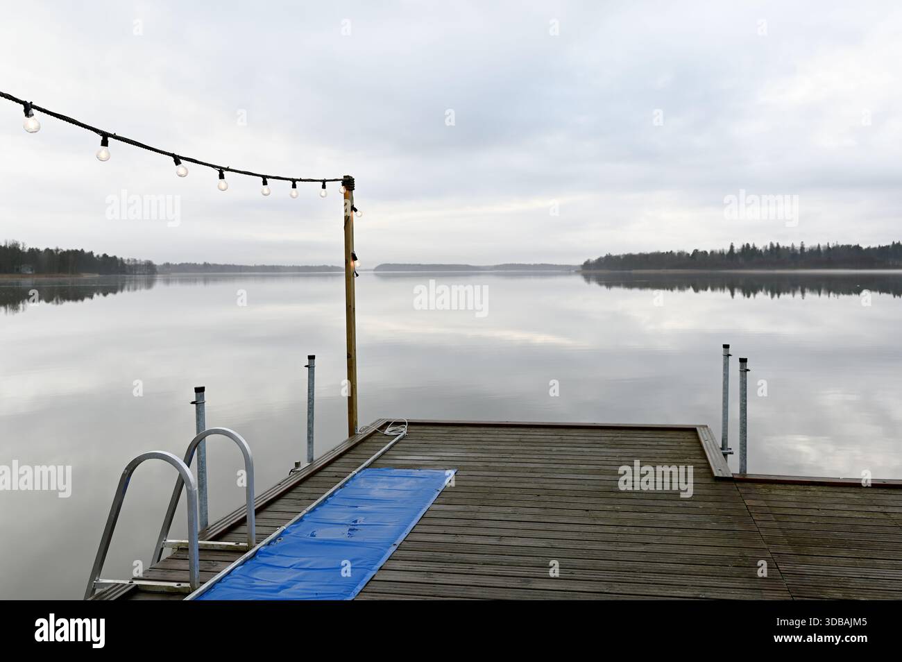 Una tranquilla scena lacustre caratterizzata da un molo in legno adornato da luci a corda morbida, che si affaccia su un lago perfettamente fermo, simile a uno specchio sotto una W ricoperta Foto Stock