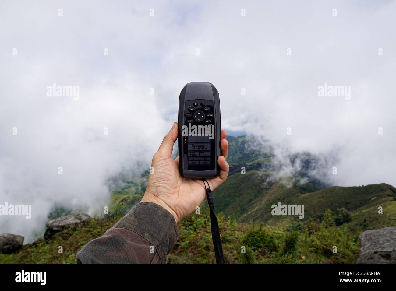 Mano che regge un dispositivo GPS portatile per navigare contro un paesaggio di montagna nebbioso durante un'avventura escursionistica. Foto Stock
