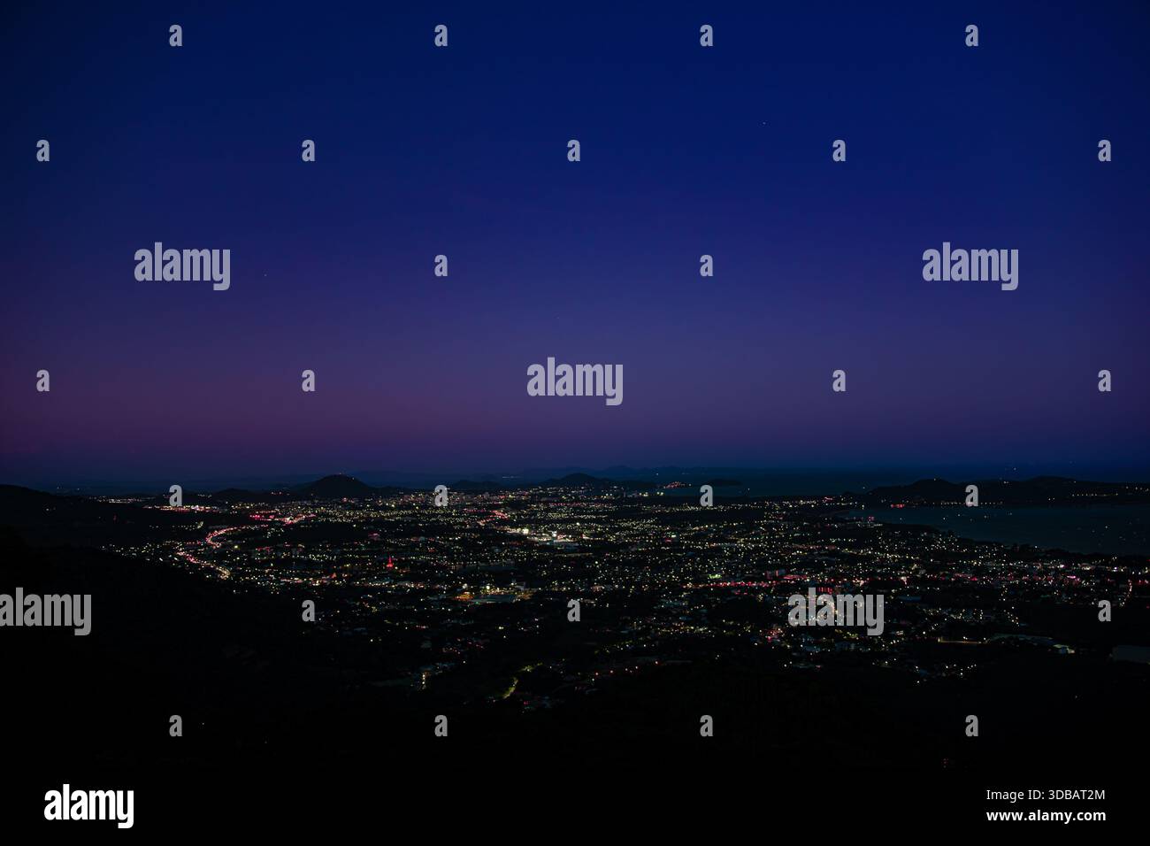 Una vista notturna mozzafiato dal punto panoramico di lussureggianti e scure colline. Sotto, la costa curva graziosamente, dove la luce elettrica si illumina. Foto Stock