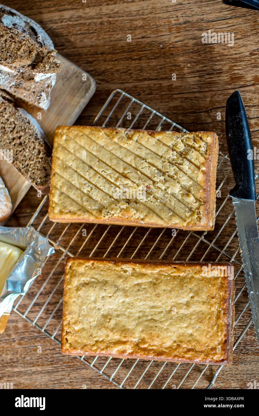 Le torte di pane rettangolari fatte in casa si raffreddano su una griglia metallica con pane e coltello su un tavolo di legno Foto Stock