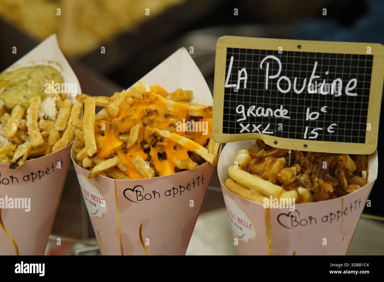 Coni di poutina e patatine fritte caricate in mostra in uno stand di Street food con un cartello del prezzo della lavagna. Nantes, Francia Foto Stock