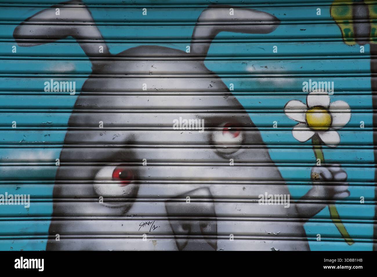 Murale di Street art di una figura di un cartone animato su un otturatore metallico che regge una margherita bianca su uno sfondo blu. Nantes, Francia Foto Stock