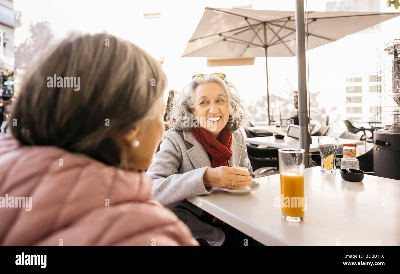 Le donne più anziane sono amiche sedute in un bar all'aperto, sorridono e parlano Foto Stock
