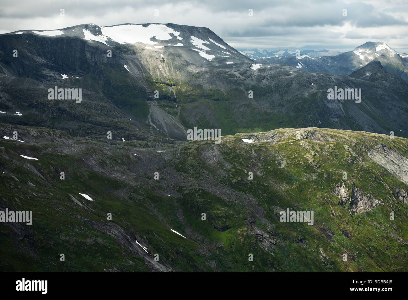Le vette innevate si innalzano su paesaggi verdi con nuvole che si muovono attraverso il cielo nella regione montuosa della Norvegia. Foto Stock