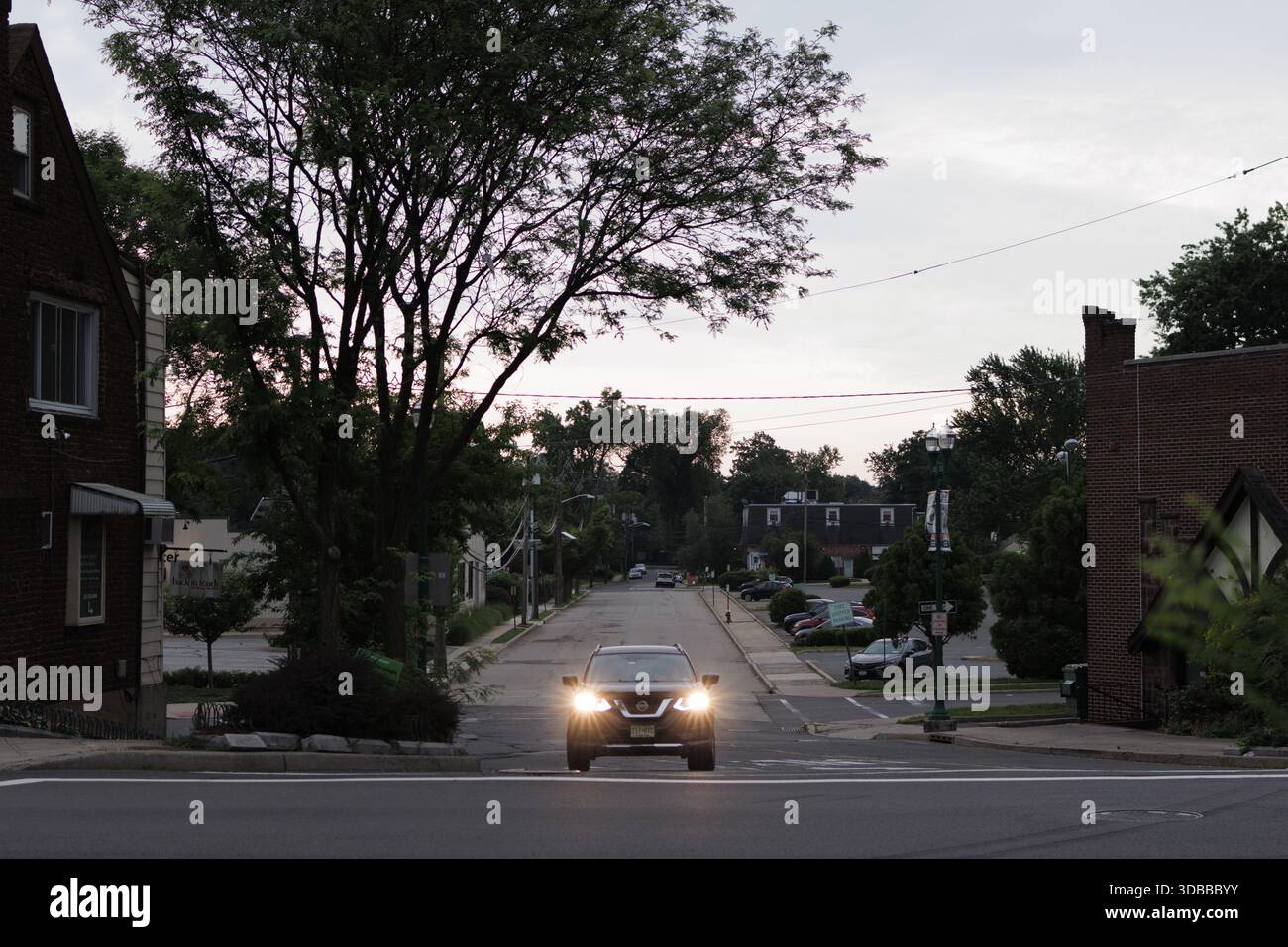 Un'auto con i fari accesi, guida dritto alla telecamera in una strada suburbana del New Jersey. Foto Stock