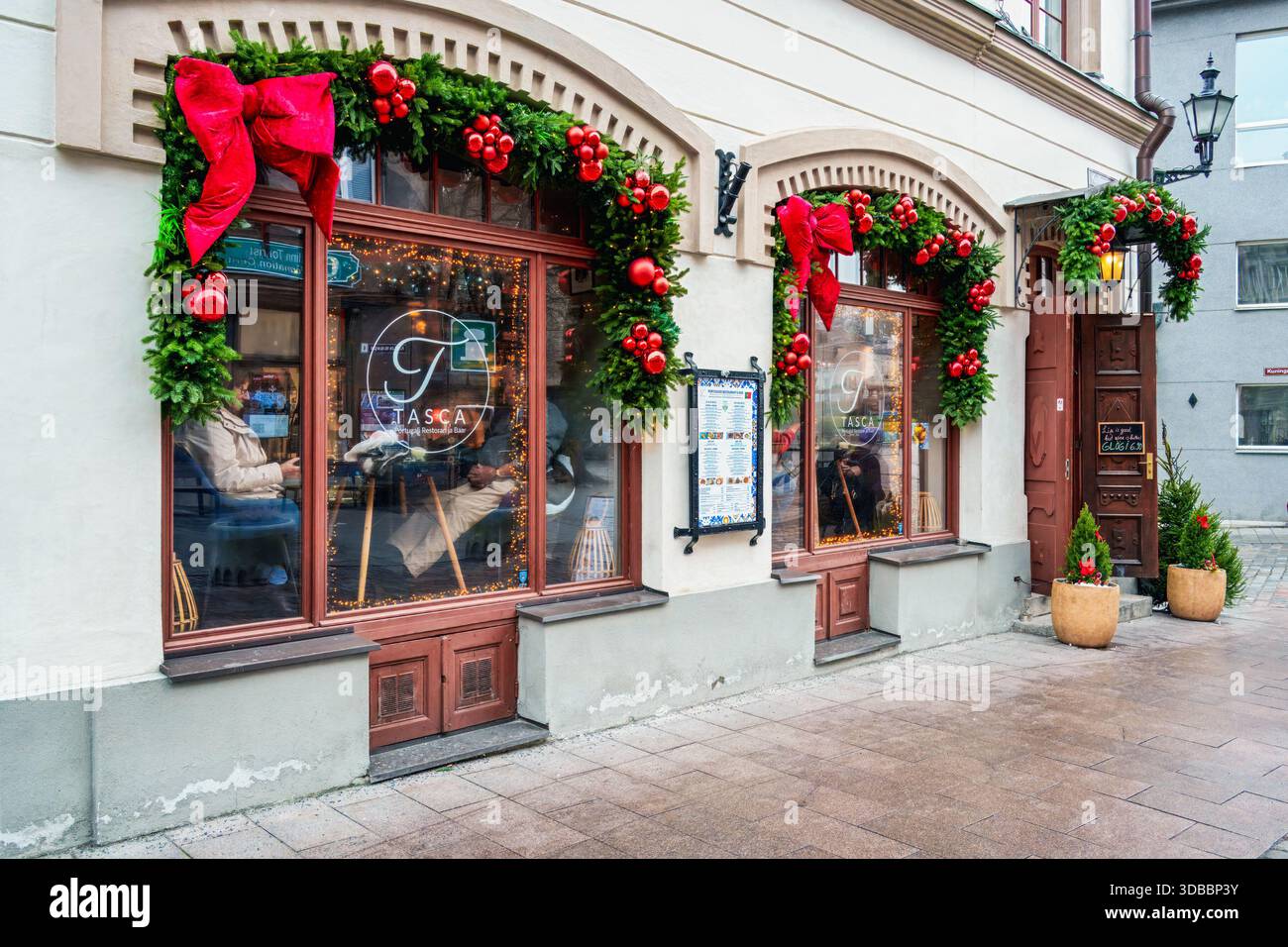 Tallinn, Estonia - 3 dicembre 2025: Finestre del ristorante splendidamente decorate con ghirlande natalizie e archi rossi, che creano una calda atmosfera di vacanza Foto Stock