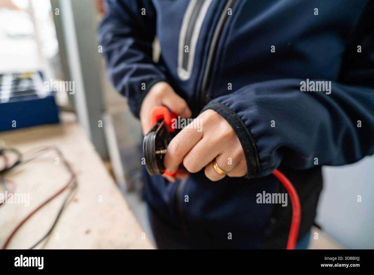 Lavorare con le mani con una pinza a crimpare su un filo elettrico rosso, creando un collegamento sicuro Foto Stock