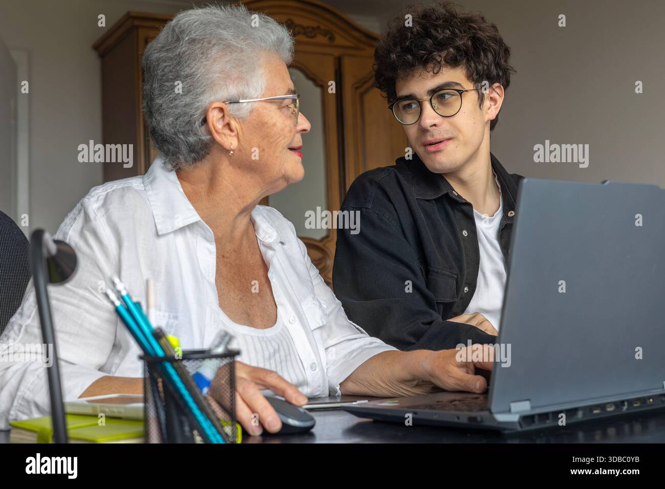 Nonna e nipote che utilizzano il laptop a casa per l'online banking, il pagamento delle fatture, la prenotazione di viaggi e l'apprendimento delle competenze digitali. Sostegno familiare, Foto Stock