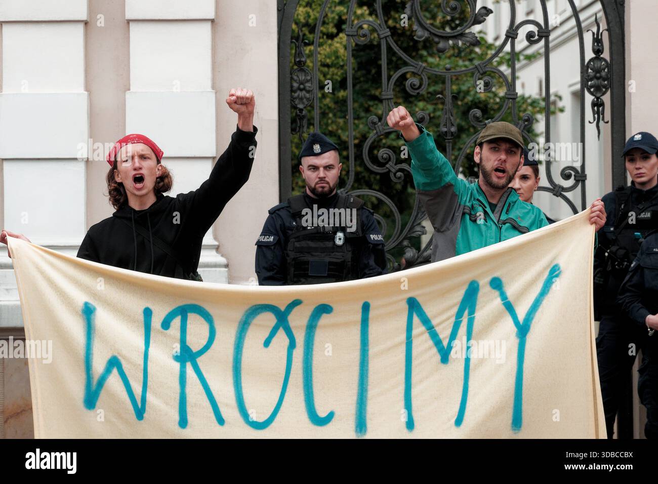 I manifestanti alzano i pugni dietro lo striscione che recita "We'll Be Back" come guardia della polizia in una manifestazione vicino all'Università di Varsavia. Foto Stock