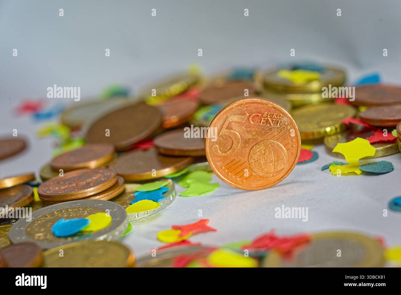 Moneta da cinque centesimi di euro circondata da coriandoli colorati che rappresentano piccoli risparmi di bilancio microfinanza e decisioni finanziarie quotidiane Foto Stock