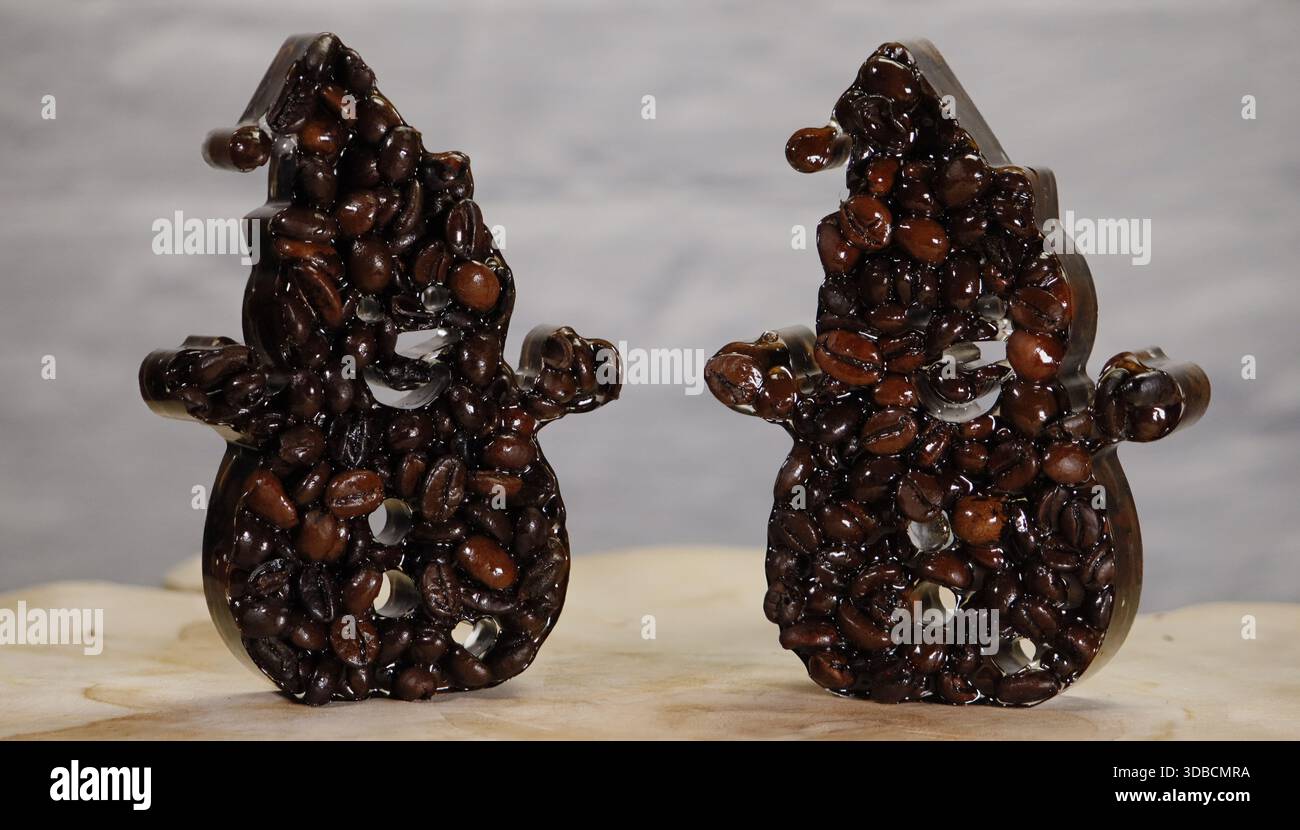 Due pupazzi di neve creati da chicchi di caffè tostati su uno sfondo chiaro. Creatività culinaria invernale che combina aroma di caffè e atmosfera festosa, ideale Foto Stock