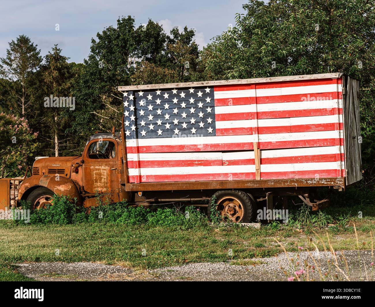 Camion Dodge d'epoca abbandonato sull'erba con una grande bandiera americana dipinta sulla scatola di legno, che documenta l'America rurale. Foto Stock