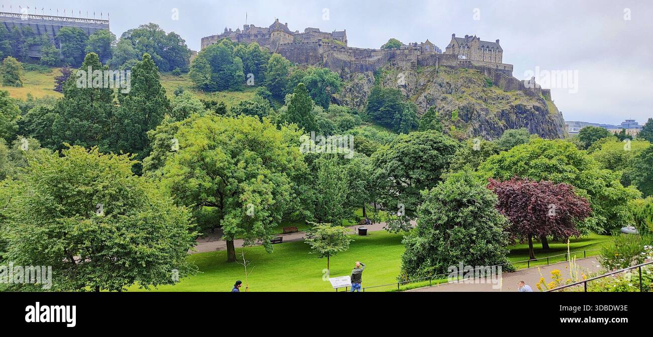 Una splendida vista del Castello di Edimburgo che torreggia sul suo arroccato roccioso, vista da Princes Street, circondata da lussureggiante vegetazione e bagnata dalla luce estiva. Foto Stock