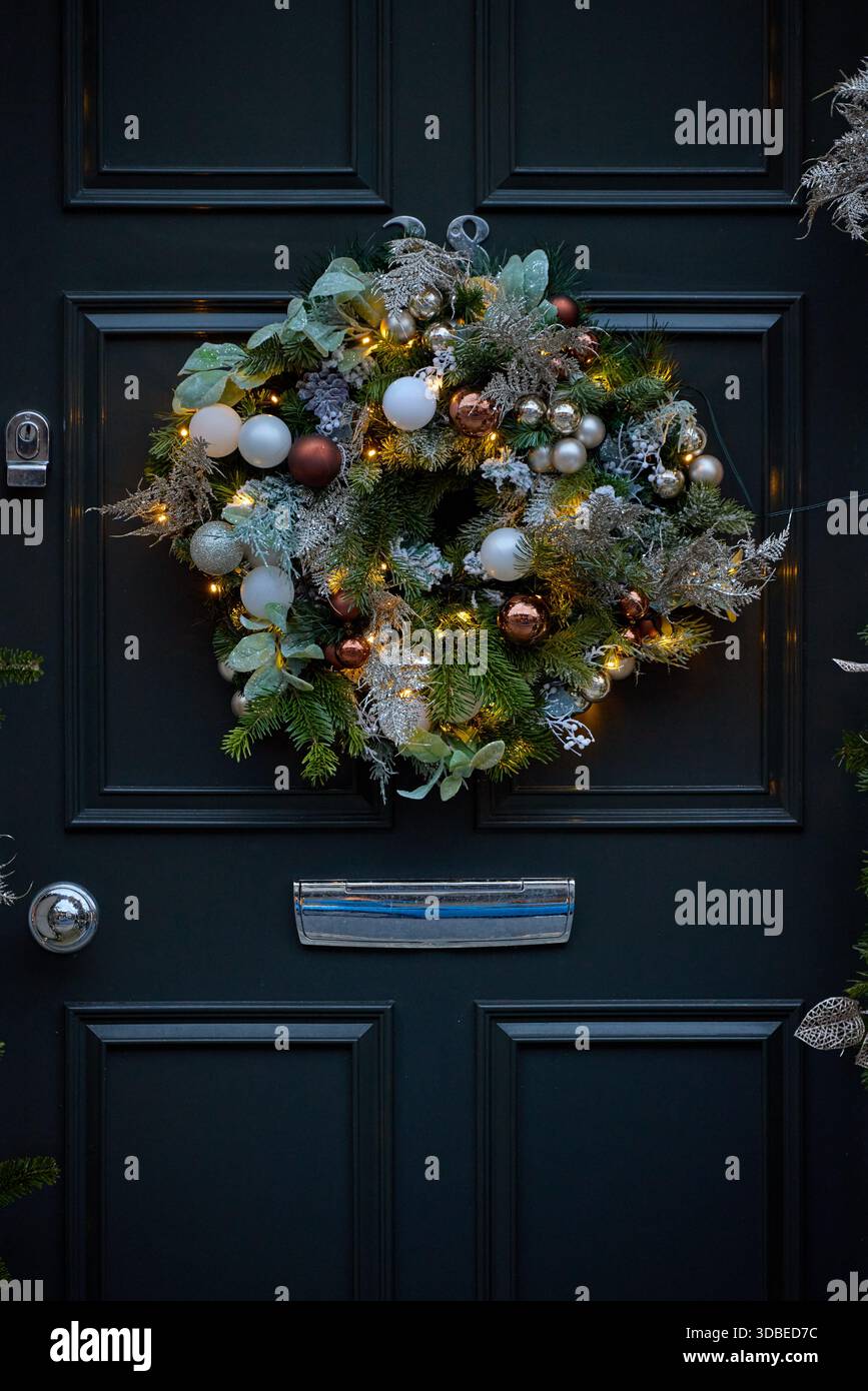 Decorazioni natalizie con ghirlande e luci e baule che incorniciano una tradizionale porta d'ingresso nera sull'esterno di una casa cittadina in pietra. Foto Stock