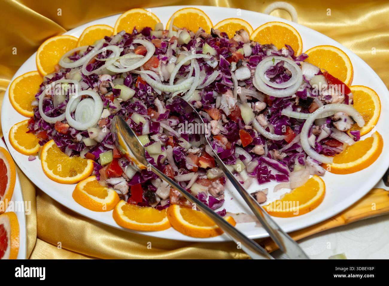 Insalata tritata colorata con cavolo rosso, pomodori, cipolle e fette d'arancia su un piatto Foto Stock