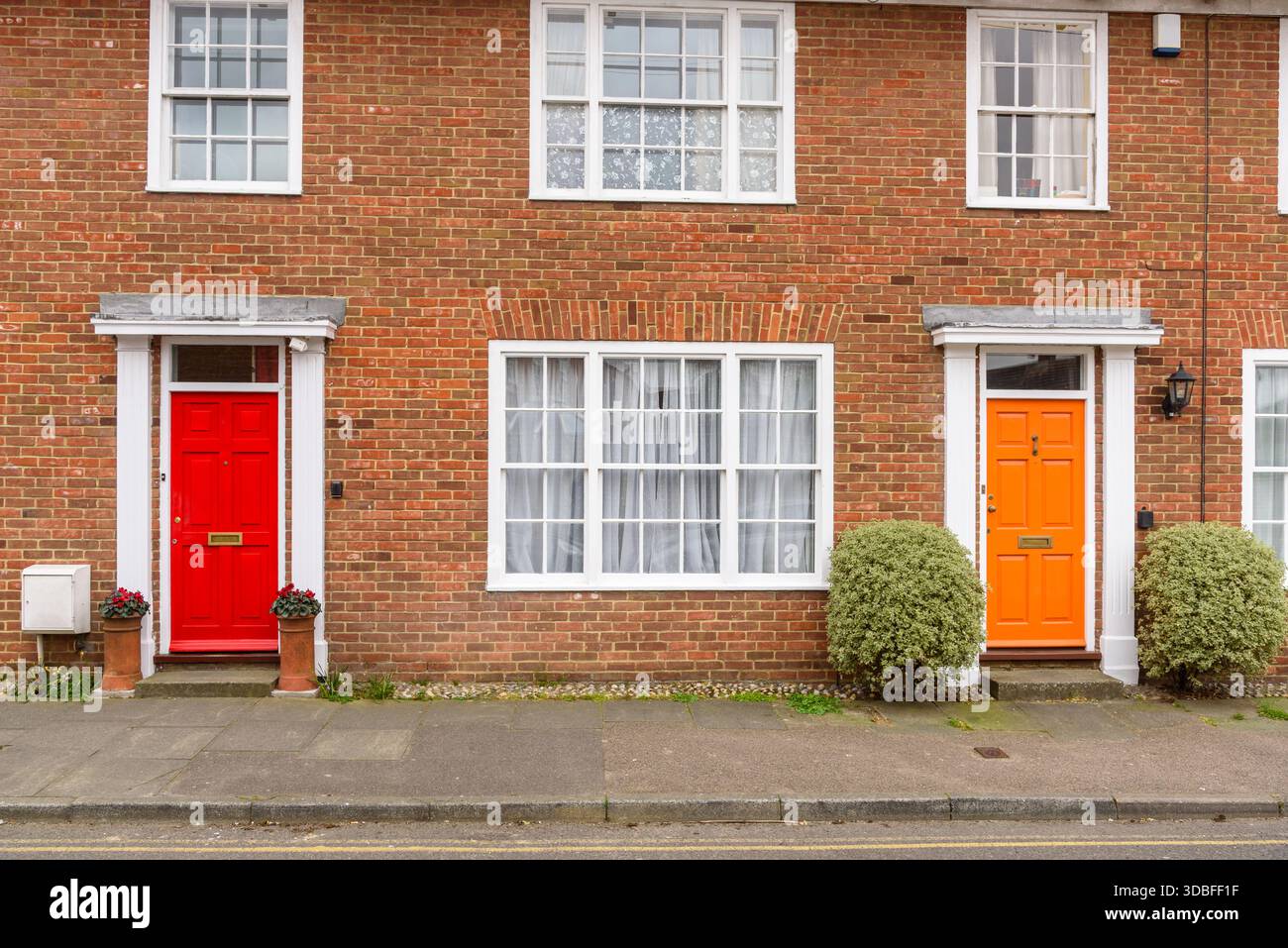 Colorate porte frontali in legno di due vecchie case terrazzate in mattoni. Una porta è di colore rosso brillante mentre l'altra è di colore arancione brillante. Foto Stock