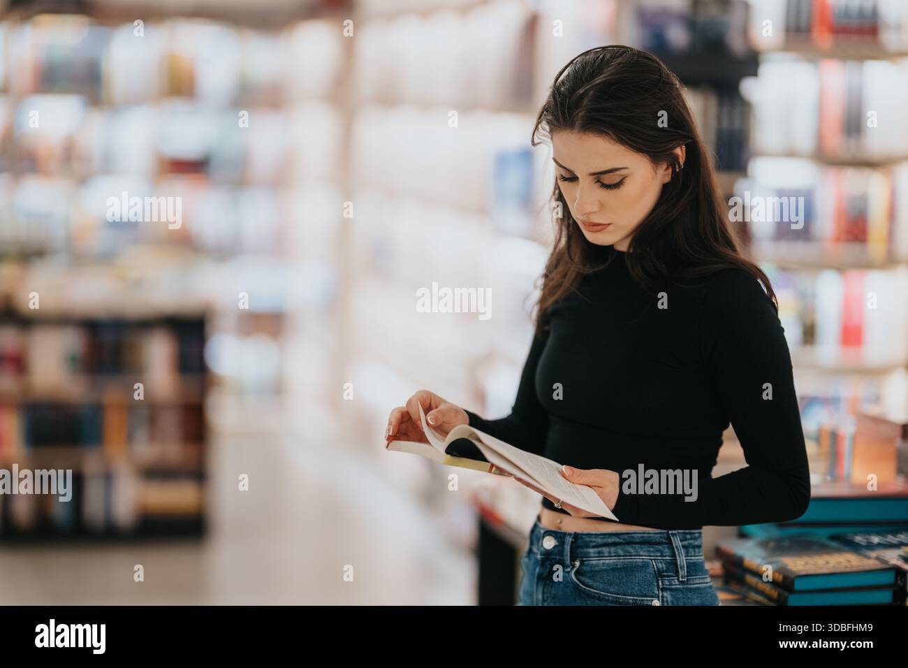 Una donna legge un opuscolo in una libreria luminosa, concentrata e calma, tra scaffali di libri Foto Stock