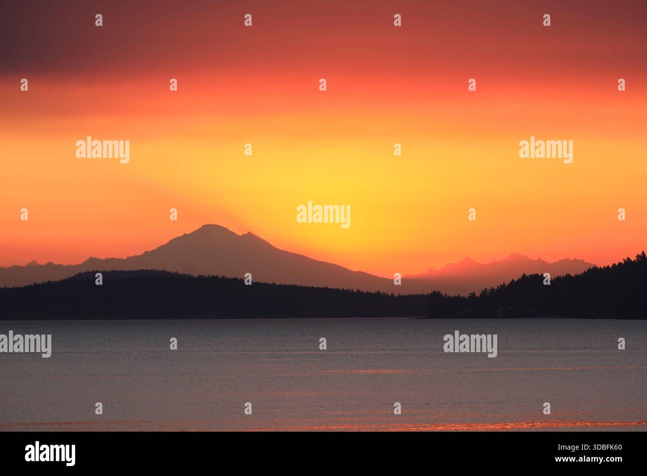 Guardando dall'Isola di Vancouver in Canada sullo dritto della Georgia, una splendida sagoma del Monte Baker contro un cielo arancione vivo. Foto Stock