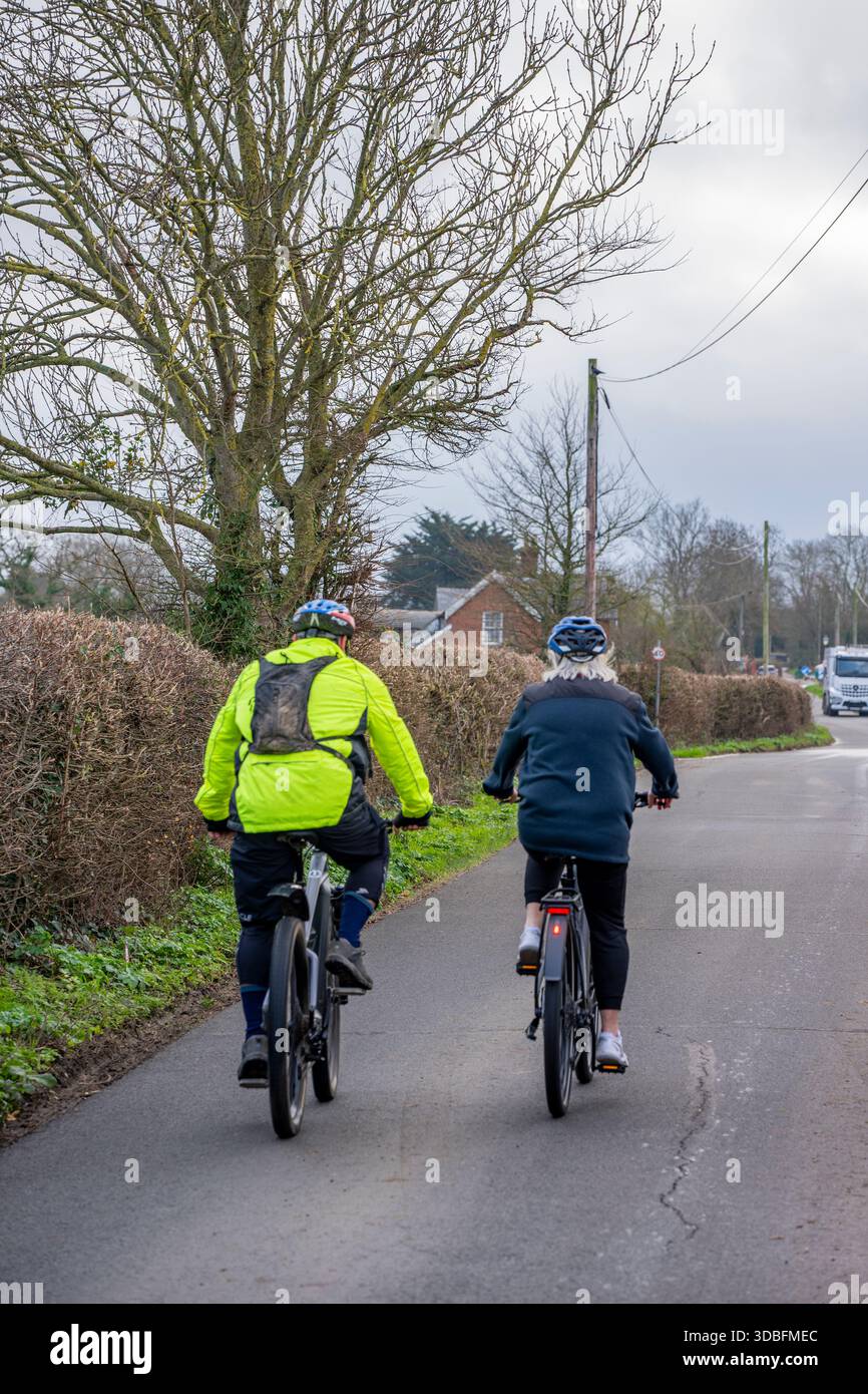 Coppie più vecchie che viaggiano in bicicletta lungo una strada di campagna insieme, coppie che vanno in bicicletta su una strada tranquilla insieme. Foto Stock