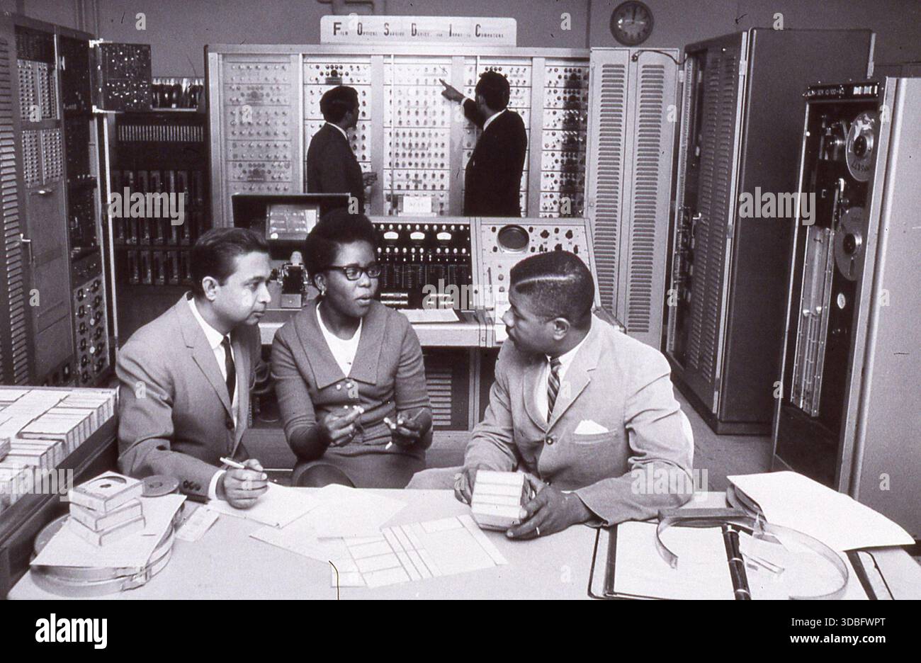 Fotografia del personale afroamericano che gestisce il Film Optical Sensing Device for input to Computers (FOSDIC) nel 1960. Il sistema FOSDIC è stato utilizzato per digitalizzare ed elaborare grandi quantità di dati, illustrando le prime tecnologie informatiche e il contributo di diversi operatori nella storia informatica degli Stati Uniti. Foto Stock